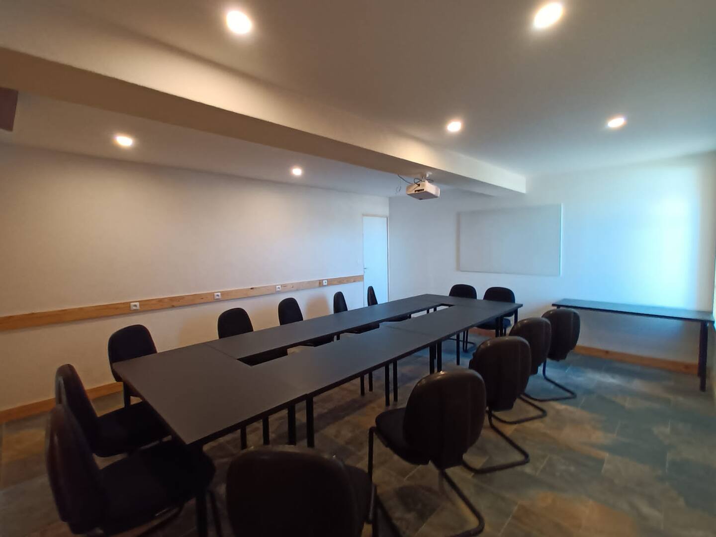Vista general de la sala de reuniones del jardín, con mesas unidas y pantalla de proyección